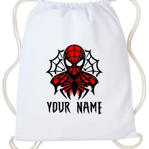 May include: White drawstring backpack featuring a red and black Spider-Man graphic. The design includes a spider web and the text "YOUR NAME" in a gothic font. The bag has white drawstrings.