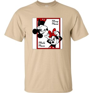 May include: A tan t-shirt featuring a graphic of Mickey Mouse and Minnie Mouse. The graphic is in a red rectangular frame with the words "Mickey Mouse" and "Minnie Mouse" in black text. Mickey is upside down, and Minnie is right-side up.