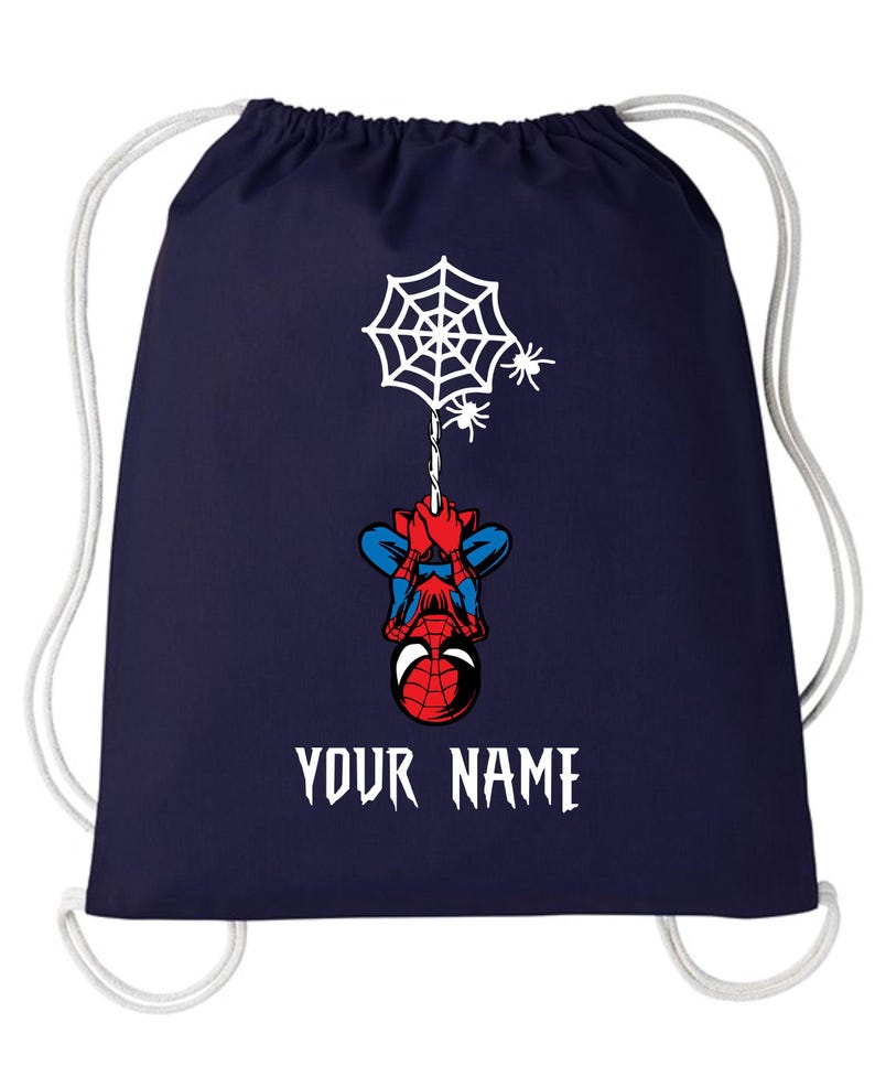 Puede incluir: Mochila con cord&oacute;n de color azul marino con un dise&ntilde;o de Spider-Man. El dise&ntilde;o incluye una telara&ntilde;a blanca, dos peque&ntilde;as ara&ntilde;as y el texto "YOUR NAME" en blanco. El superh&eacute;roe est&aacute; colgado boca abajo. Cierre con cord&oacute;n blanco.