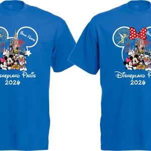 May include: Two blue t-shirts with a Disneyland Paris 2026 design. The design features Mickey and Minnie Mouse, Donald Duck, and other Disney characters. One shirt has a red bow, and both have a white Mickey Mouse head outline with fireworks and text.