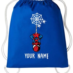 Puede incluir: Mochila con cord&oacute;n azul con un dise&ntilde;o de Spider-Man colgando de una telara&ntilde;a con dos ara&ntilde;as. La mochila tiene cordones blancos y el texto "YOUR NAME" en blanco.