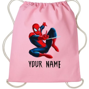 May include: A pink drawstring backpack featuring a colorful illustration of Spider-Man in action. The superhero is depicted in his classic red and blue suit. The text "YOUR NAME" is printed in black below the image.