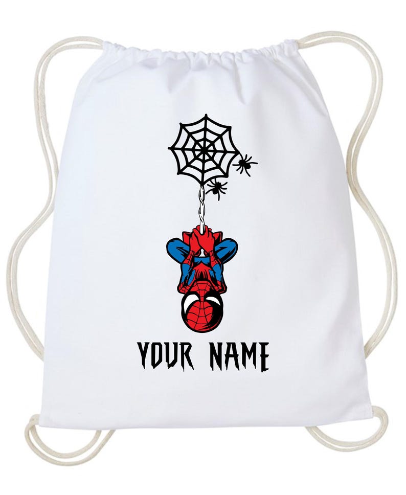 Puede incluir: Mochila con cord&oacute;n blanca con un dise&ntilde;o de Spiderman. El dise&ntilde;o incluye una telara&ntilde;a negra, dos peque&ntilde;as ara&ntilde;as y Spiderman colgado boca abajo. El texto "YOUR NAME" est&aacute; impreso en negro debajo.