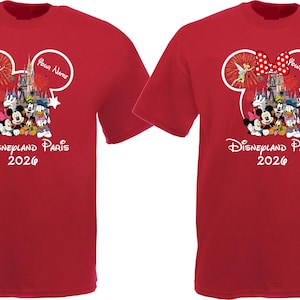 May include: Two red t-shirts with a Disney theme. Each shirt features a Mickey Mouse head outline with a castle, characters, and the text "Disneyland Paris 2026." One shirt has a red bow with white polka dots.
