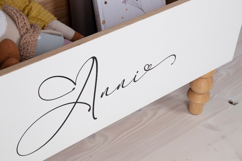 May include: White wooden storage box with a cursive inscription that reads "Annie" with a small heart symbol. The box has wooden legs.