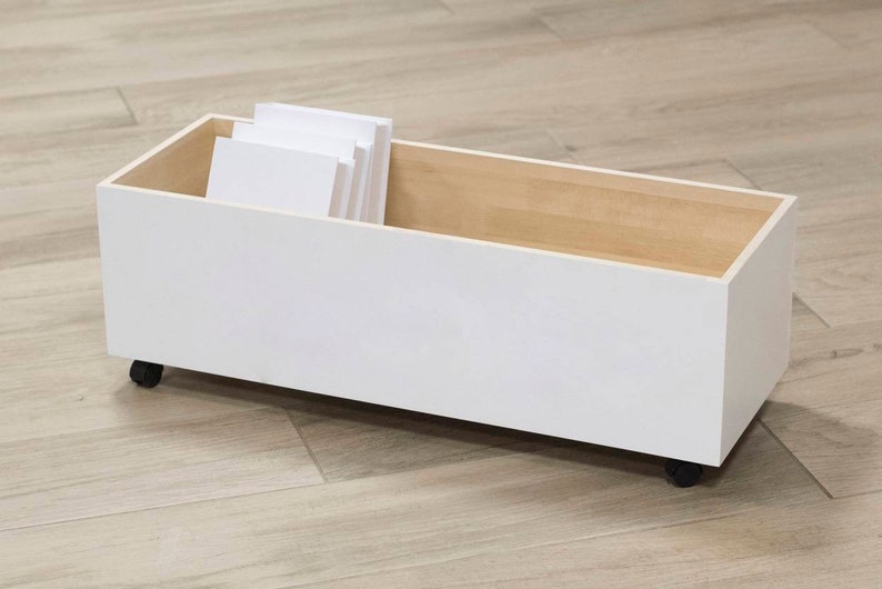 May include: White storage box with wheels and a wooden top. The box is filled with white paper.
