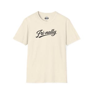 May include: Cream-colored t-shirt with the word "Fri-nally" in black script across the front. The shirt has a crew neck and short sleeves. The fabric has a speckled texture.