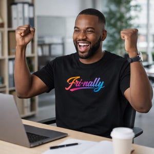 May include: A black t-shirt with the word "Fri-nally" in a gradient of orange, pink, and blue. The person wearing the shirt is smiling and has their fists clenched in the air.
