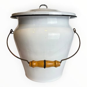 May include: A white enamel bucket with a matching lid, featuring a thin black rim around the top edge. The bucket has a curved metal wire handle attached to the sides, which includes a central wooden grip with a small black band in the middle.