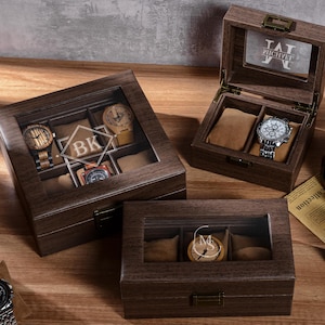 Könnte beinhalten: Uhren-Displayboxen aus Holz mit Glasdeckeln. Eine Box ist geöffnet und zeigt eine Uhr. Eine andere Box hat die Initialen "BK" darin. Ein Grammophon im Vintage-Stil und eine brennende Kerze sind ebenfalls sichtbar.