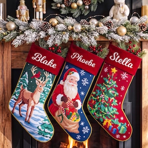 Könnte beinhalten: Drei personalisierte Weihnachtsstrümpfe mit roten Samtstulpen, die die Namen Blake, Phoebe und Stella tragen. Die Strümpfe zeigen Stickmotive eines Hirsches in einem verschneiten Wald, des Weihnachtsmanns mit Geschenkesack und eines Tannenbaums.
