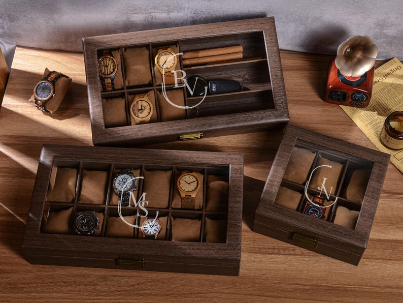 Puede incluir: Cajas de exhibici&oacute;n de relojes de madera con tapas de vidrio. Las cajas est&aacute;n llenas de varios relojes y almohadas para relojes. Una caja tiene un compartimento para puros y una llave de coche. Las cajas est&aacute;n grabadas con iniciales.