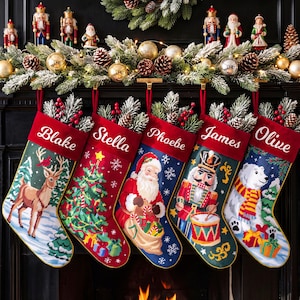 May include: Five Christmas stockings with red cuffs featuring the names Blake, Stella, Phoebe, James, and Olive. The stockings display festive needlepoint designs including a reindeer, a Christmas tree, Santa Claus, a nutcracker, and a polar bear.