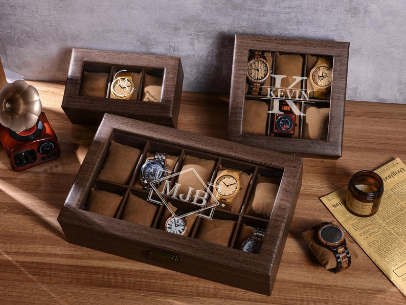 Puede incluir: Cajas de exhibici&oacute;n de relojes de madera con tapas de vidrio, que muestran varios relojes de pulsera. Las cajas son marrones con compartimentos individuales forrados con tela marr&oacute;n. Una caja tiene las iniciales "MJB" y otra el nombre "KEVIN" en el cristal.