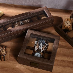 Puede incluir: Cajas de madera para relojes con tapas transparentes, que muestran varios relojes. Una caja est&aacute; abierta, revelando compartimentos para relojes. Las cajas est&aacute;n grabadas con nombres. Se muestra un reloj de madera.