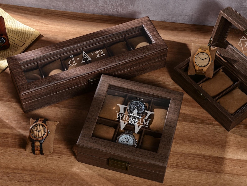 Puede incluir: Cajas de madera para relojes con tapas transparentes, que muestran varios relojes. Una caja est&aacute; abierta, revelando compartimentos para relojes. Las cajas est&aacute;n grabadas con nombres. Se muestra un reloj de madera.
