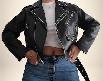 May include: Black leather jacket with silver stud accents. The jacket features a classic asymmetrical zipper closure, multiple pockets, and a belt. The jacket is worn over a white top and blue jeans.