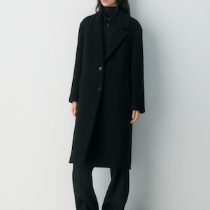 May include: A long, black coat with a classic lapel collar and button closure. The coat is paired with black trousers and a black top. The outfit is simple and elegant, suitable for various occasions.