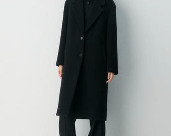Puede incluir: Un abrigo largo negro con cuello de solapa clásico y cierre de botones. El abrigo se combina con pantalones negros y una parte superior negra. El atuendo es simple y elegante, adecuado para diversas ocasiones.