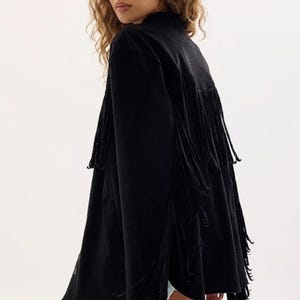 May include: Black jacket with long fringe detailing. The jacket has a high collar and a loose fit. The fringe is long and hangs down from the back and sleeves. The jacket is made of a soft, flowing fabric.