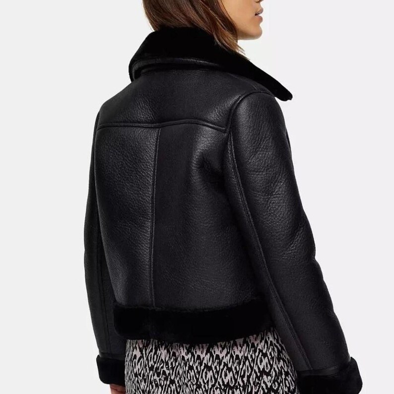 May include: Black faux leather jacket with a shearling collar and trim. The jacket features a classic aviator style with a notched lapel and a slightly cropped length. The jacket has a textured appearance and a warm, cozy look.