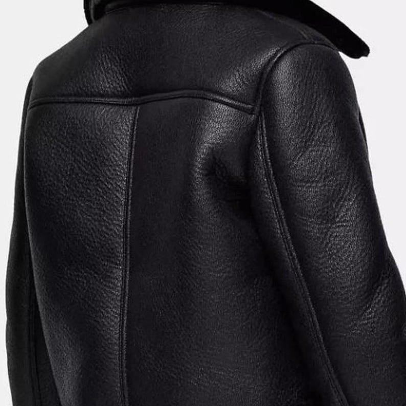 May include: Close-up of a black leather jacket with a shearling collar. The jacket has a textured surface and visible stitching details. The back of the jacket is shown, highlighting the design and construction of the garment.
