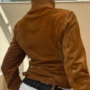 Pode incluir: Casaco de camur&ccedil;a castanho com gola alta e silhueta ajustada. O casaco apresenta fecho de correr e detalhe de cinto na cintura. As mangas s&atilde;o compridas e o casaco parece bem usado.