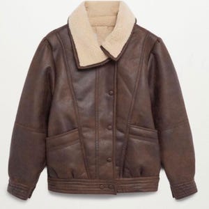 May include: A brown faux leather jacket with a cream-colored shearling collar. The jacket has a button-up front, two front pockets, and ribbed cuffs. The jacket is a bomber style.