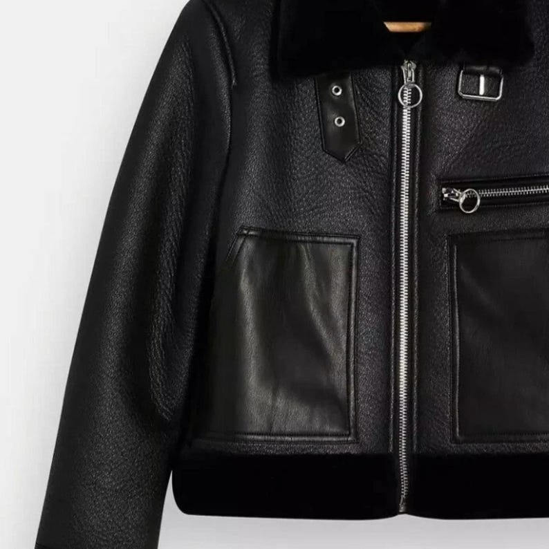 May include: Black faux leather jacket with a shearling collar and lining. Features include a front zipper, two front pockets, and decorative silver hardware. The jacket has a classic aviator style.