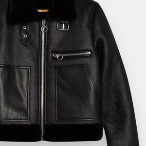 May include: Black faux leather jacket with a shearling collar and lining. The jacket features a zip-up front, two front pockets, and decorative silver hardware. The jacket has a classic aviator style.