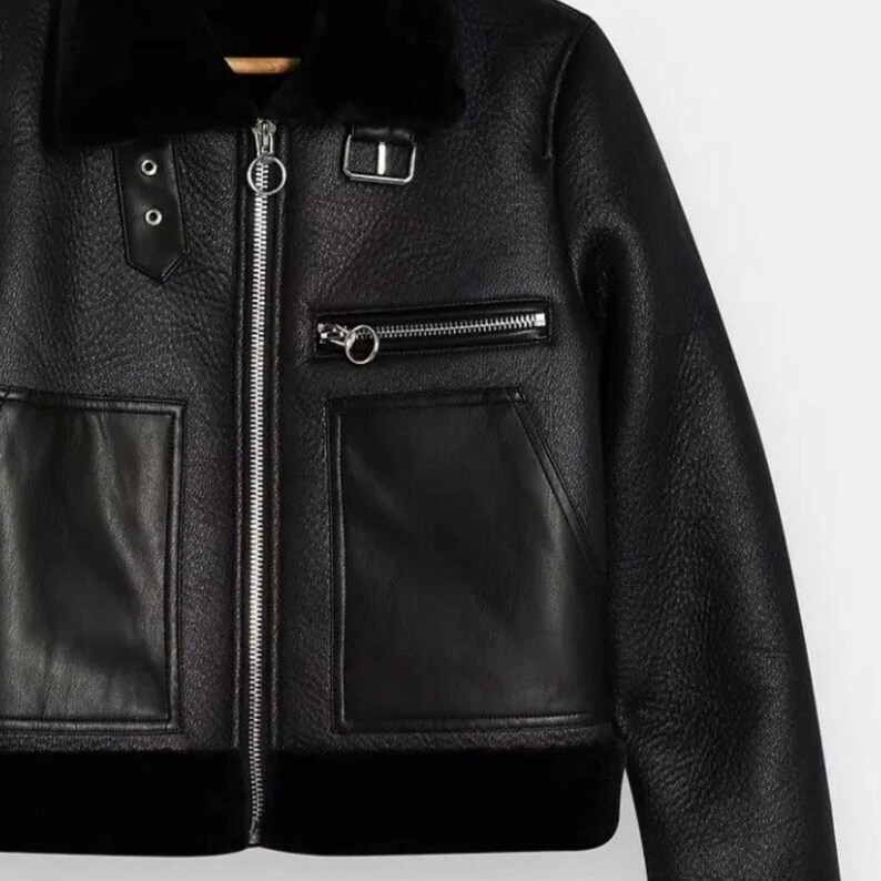May include: Black faux leather jacket with a shearling collar and lining. The jacket features a zip-up front, two front pockets, and decorative silver hardware. The jacket has a classic aviator style.