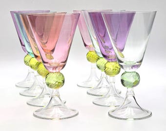May include: A set of six glass goblets featuring translucent bowls in shades of pink, purple, and teal. Each stem includes a decorative, textured lime green glass sphere accent above a clear, flared circular base for stability and support.