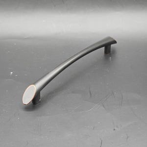 May include: A curved, matte black cabinet pull with copper-colored end caps. The handle is arched and has a sleek, modern design. This hardware is suitable for drawers and cabinets.