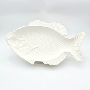 May include: A white ceramic serving dish shaped like a fish. The surface features a textured scale pattern across the body, with molded details for the fins, tail, and head. The dish has a smooth, glossy finish and a defined eye and gill area.