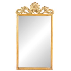 May include: A rectangular wall mirror with a gold-toned wooden frame. The top of the frame features an ornate, carved crest with a central shell motif flanked by symmetrical scrolling foliage patterns, providing a decorative finish.