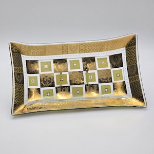 May include: A rectangular glass tray featuring a gold and olive green checkerboard pattern. The design includes alternating squares with sun, lyre, and column motifs, framed by a white border with small dots and a wide gold decorative edge.