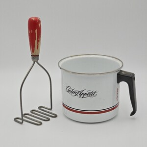 May include: A vintage kitchen set featuring a potato masher with a red handle and a white enamel mug. The mug has a black handle, a red stripe, and the words "Guten Appetit" in black script.