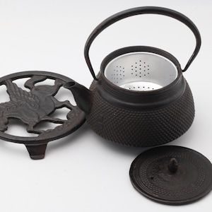 Pode incluir: Bule de ferro fundido preto com tampa e descanso de panela a condizer. O bule tem uma superfície texturizada e uma pega de metal. O descanso de panela apresenta um design de Pégaso. A tampa é redonda com um pequeno botão.