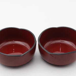 以下が含まれることがあります： 光沢のある仕上げと波状の縁を持つ2つの赤い漆器のボウル。 ボウルは暗い縁と滑らかな内部を持っています。 ボウルは、食べ物を提供したり、装飾品として使用したりする可能性があります。