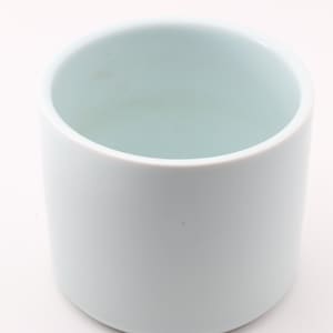 Puede incluir: Una taza cilíndrica de cerámica azul claro con un acabado liso y mate. El interior tiene un tono azul ligeramente más claro. La taza está vacía y sobre un fondo blanco. El diseño es simple y moderno.