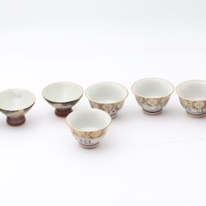 Op de afbeelding: Een verzameling van acht kleine, decoratieve keramische kommen. De kommen hebben een witte binnenkant en een patroon aan de buitenkant met gouden en bruine accenten. Elke kom heeft een diameter van ongeveer 7.6 cm en is 5 cm hoog.