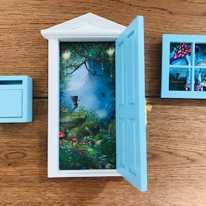 Puede incluir: Una escena en miniatura de fantasía con una puerta, una ventana y un buzón de color azul claro. La puerta abierta revela una escena de bosque con un hada. La ventana muestra setas. El buzón está a la izquierda.