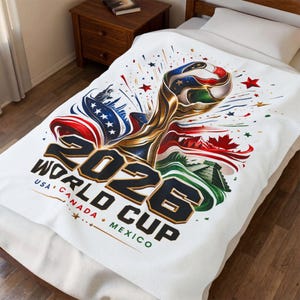 May include: White blanket featuring a gold trophy design with red, white, and blue accents, and the text "2026 WORLD CUP USA CANADA MEXICO". The design includes stars, flags, and a soccer ball.