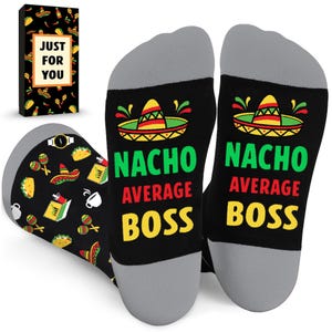 May include: Black socks with gray heels and toes, featuring a sombrero design and the text "NACHO AVERAGE BOSS" in green, red, and yellow. The socks are decorated with tacos, watches, and other Mexican-themed graphics. A gift box with the text "JUST FOR YOU" is also visible.