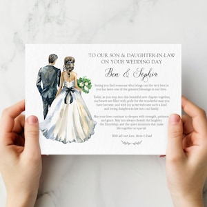Puede incluir: Una tarjeta de boda rectangular con una ilustraci&oacute;n en acuarela de una pareja con ropa formal. El texto dice: TO OUR SON & DAUGHTER-IN-LAW ON YOUR WEDDING DAY, Ben & Sophia, seguido de un mensaje y firmado con With all our love, Mom & Dad.