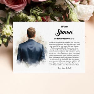 Puede incluir: Una tarjeta rectangular con una ilustraci&oacute;n en acuarela de una persona vista desde atr&aacute;s, vistiendo una chaqueta de traje azul oscuro. El texto dice: TO OUR Simon ON YOUR WEDDING DAY, seguido de un mensaje afectuoso, firmado Love Mom & Dad.