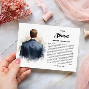 Puede incluir: Una tarjeta de boda rectangular con una ilustraci&oacute;n en acuarela de una persona vista desde atr&aacute;s con un traje azul oscuro. El texto dice: TO OUR Simon ON YOUR WEDDING DAY, seguido de un mensaje sincero, firmado Love Mom & Dad.