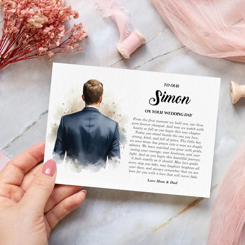 Puede incluir: Una tarjeta de boda rectangular con una ilustraci&oacute;n en acuarela de una persona vista desde atr&aacute;s con un traje azul oscuro. El texto dice: TO OUR Simon ON YOUR WEDDING DAY, seguido de un mensaje sincero, firmado Love Mom & Dad.
