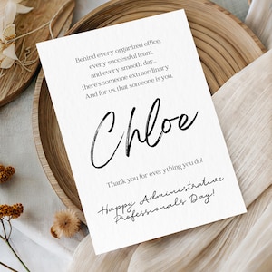 May include: A white card with black text, featuring the name "Chloe" in cursive. The card includes the phrases "Thank you for everything you do!" and "Happy Administrative Professionals Day!" It rests on a wooden tray with a neutral fabric background.