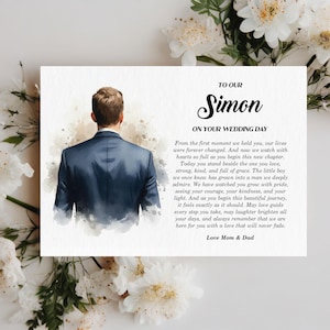 Puede incluir: Una tarjeta rectangular con una ilustraci&oacute;n en acuarela de una persona vista desde atr&aacute;s, vistiendo una chaqueta de traje azul oscuro. El texto dice: TO OUR Simon ON YOUR WEDDING DAY, seguido de un mensaje de los padres, firmado Love Mom & Dad.